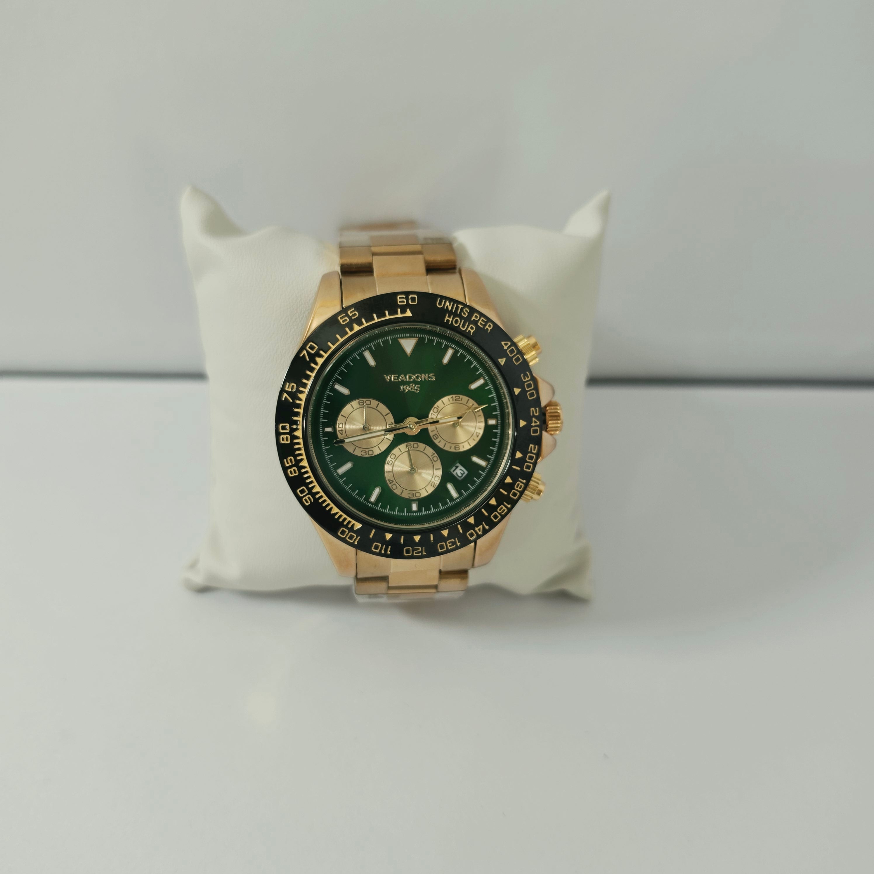  gold-tone chronograph watch with green dial displayed on a jewelry pillow

