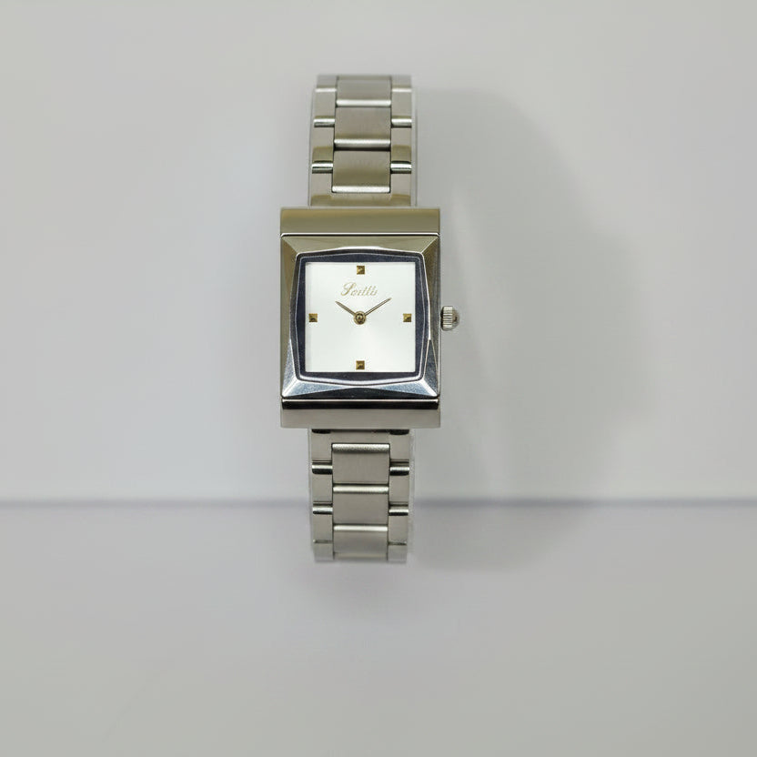 A silver-tone metal wristwatch with a square face and matching metal link bracelet, displayed upright on a clear acrylic stand against a plain light background.