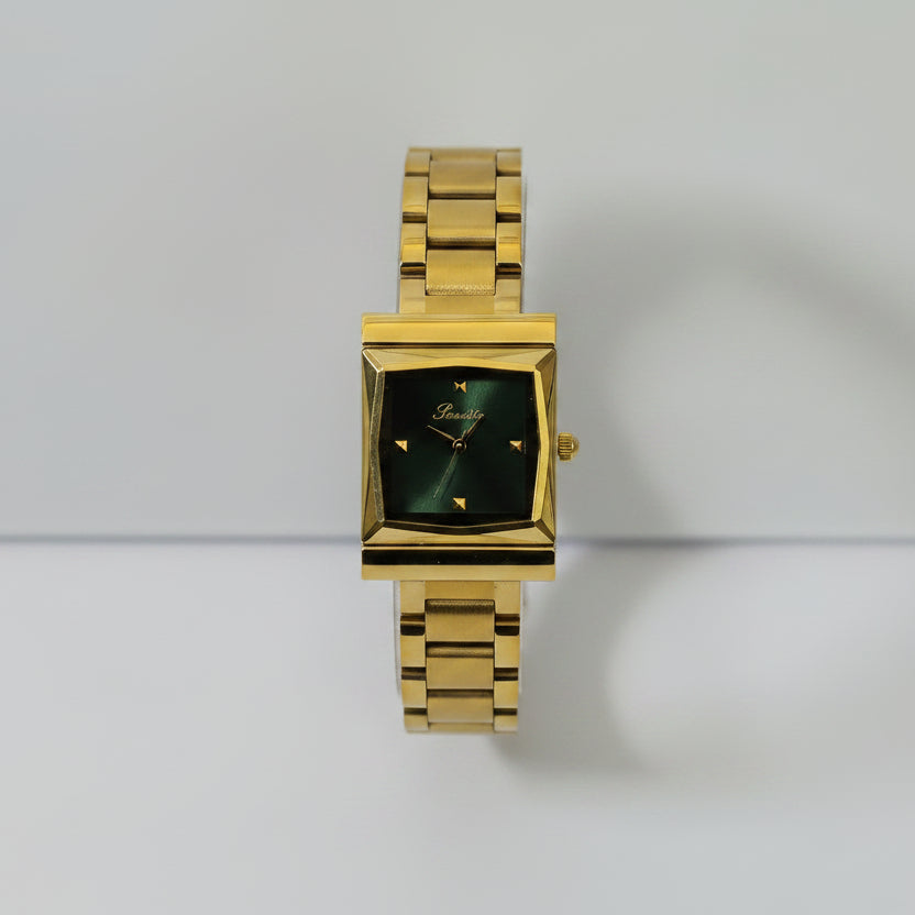 A gold-tone women's watch with a square dark green dial and a matching gold-tone metal link bracelet, displayed on a clear acrylic stand against a light gray background.