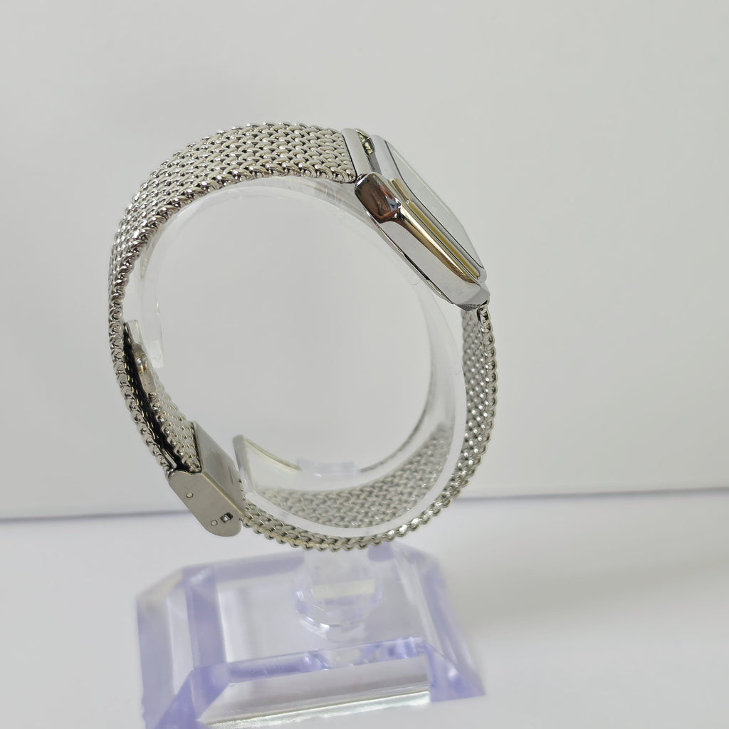 A silver-tone mesh watch band with a matching silver watch case, displayed on a clear acrylic stand against a plain white background.