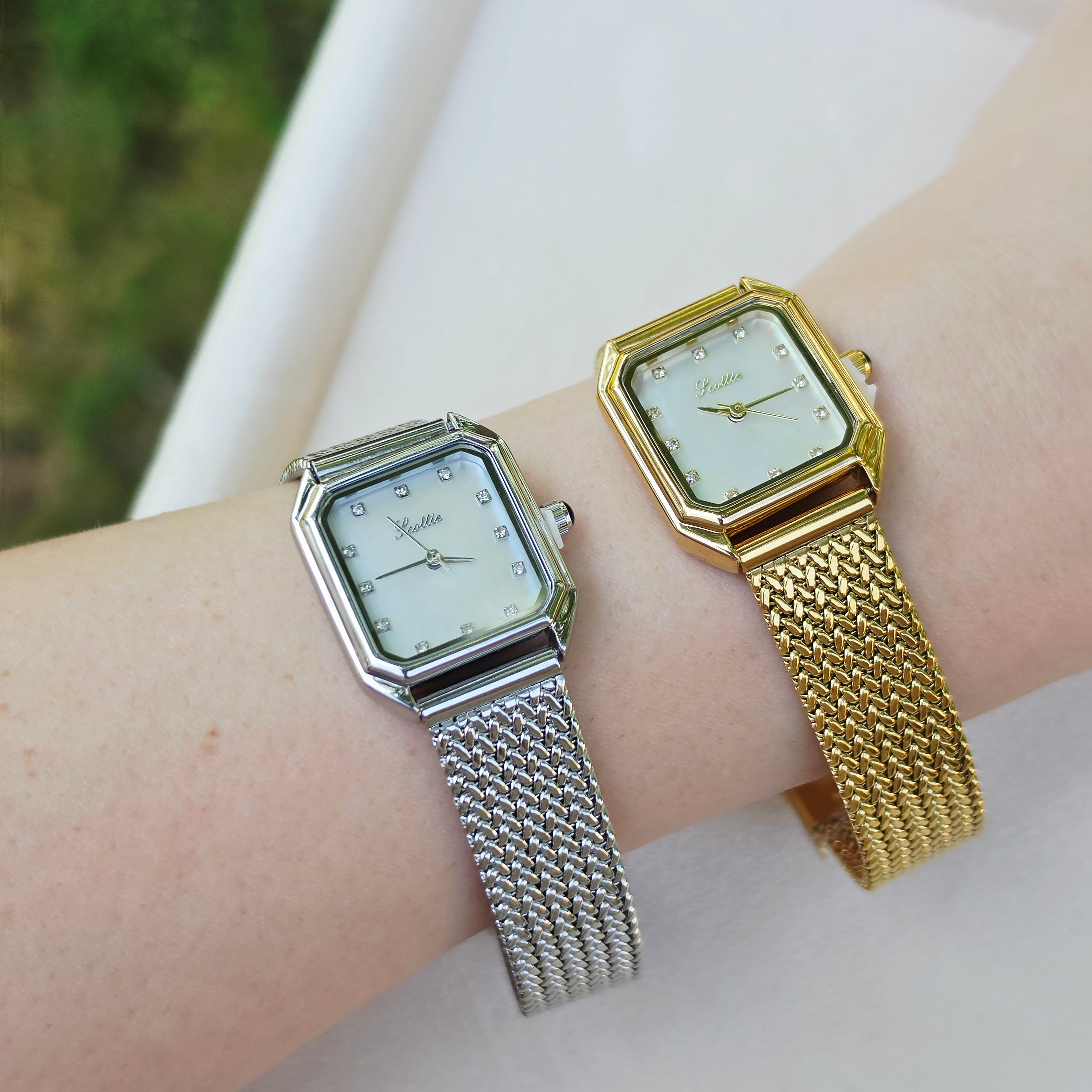 Two women's analog wristwatches with octagonal silver and gold-tone cases and mesh straps, shown on a person's wrist against a light neutral background.