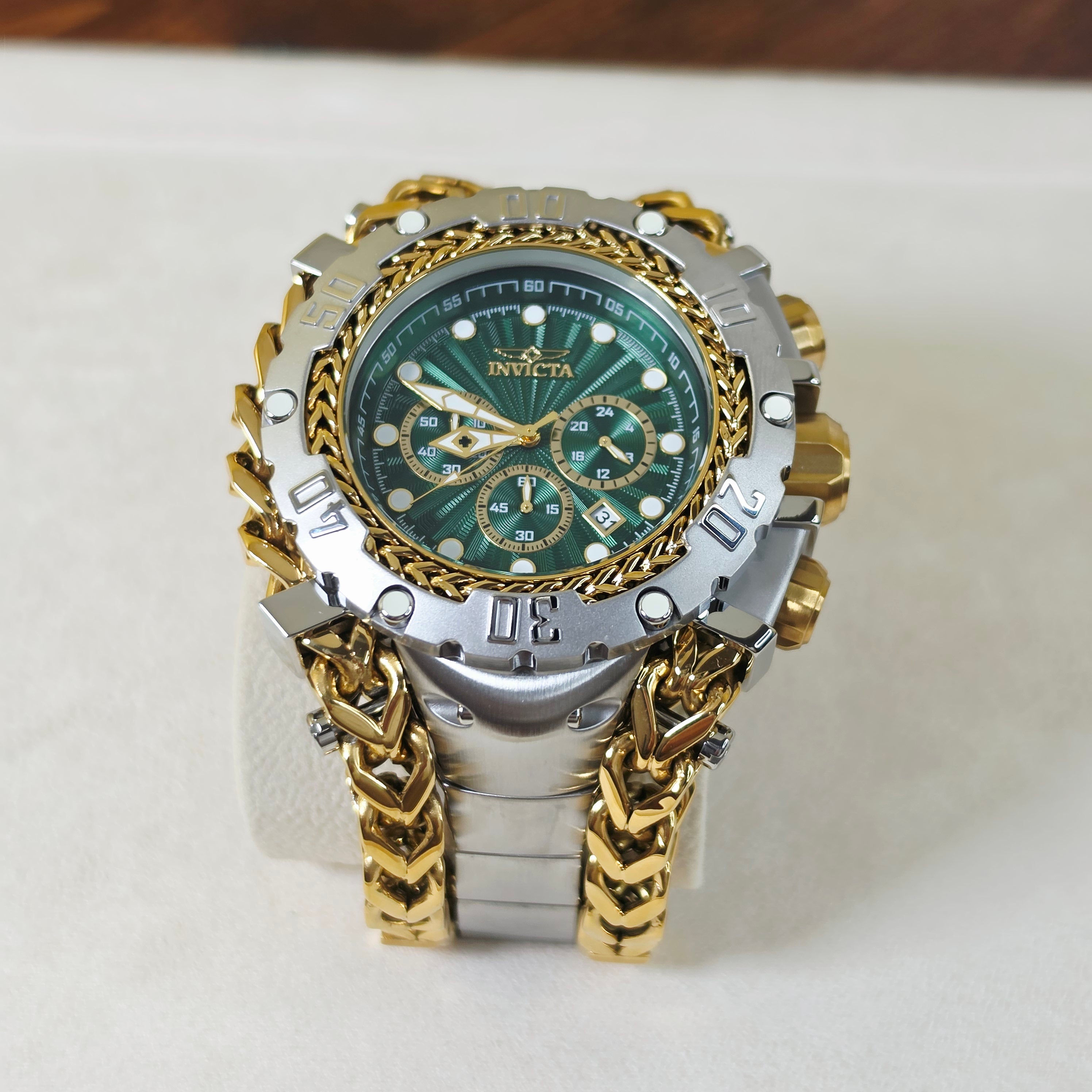 An Invicta men's watch featuring a two-tone silver and gold-tone case, a green dial with gold accents, and a matching gold and silver chain link bracelet, displayed on a white stand.