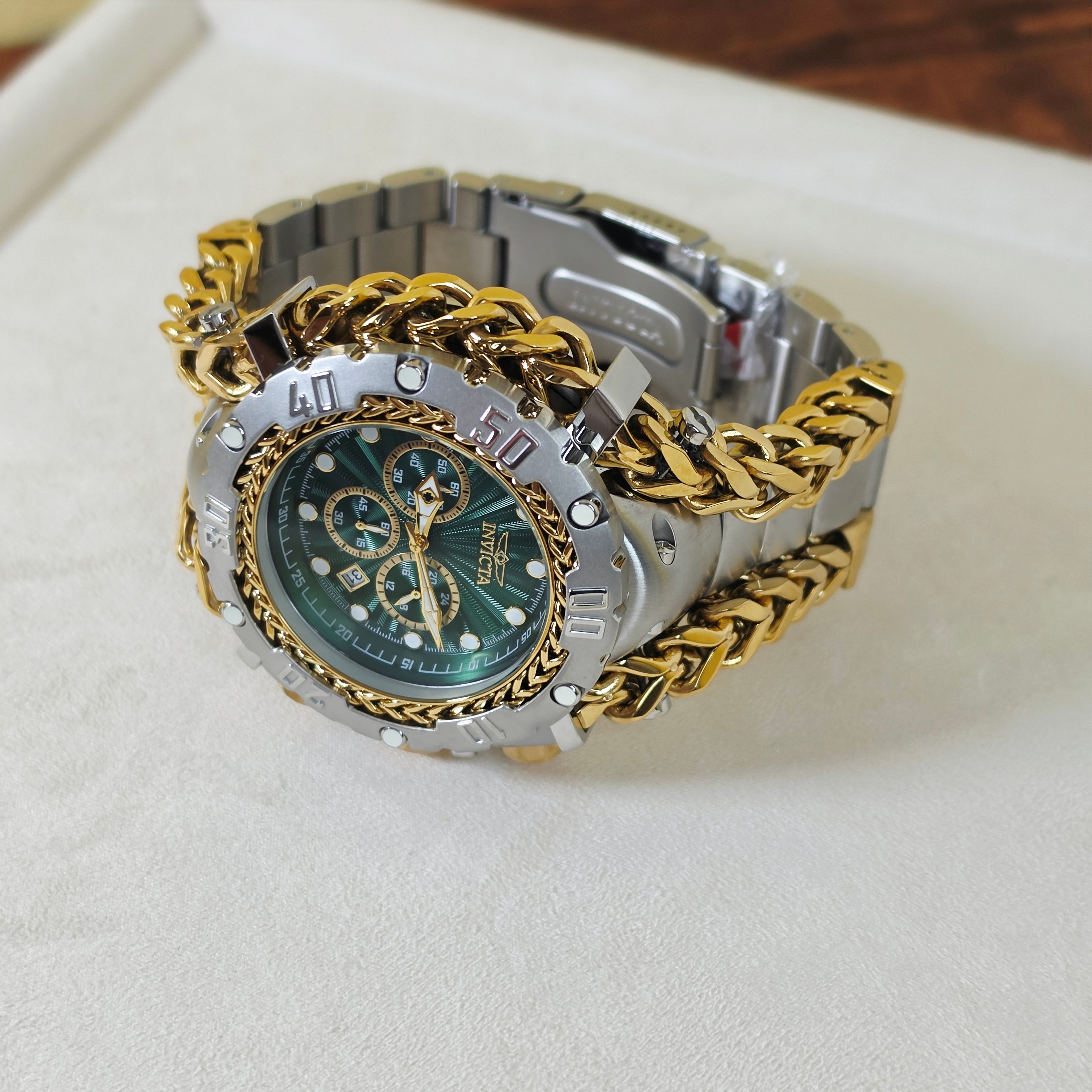 A two-tone stainless steel and gold-tone wristwatch with a green dial, resting on a white textured surface.