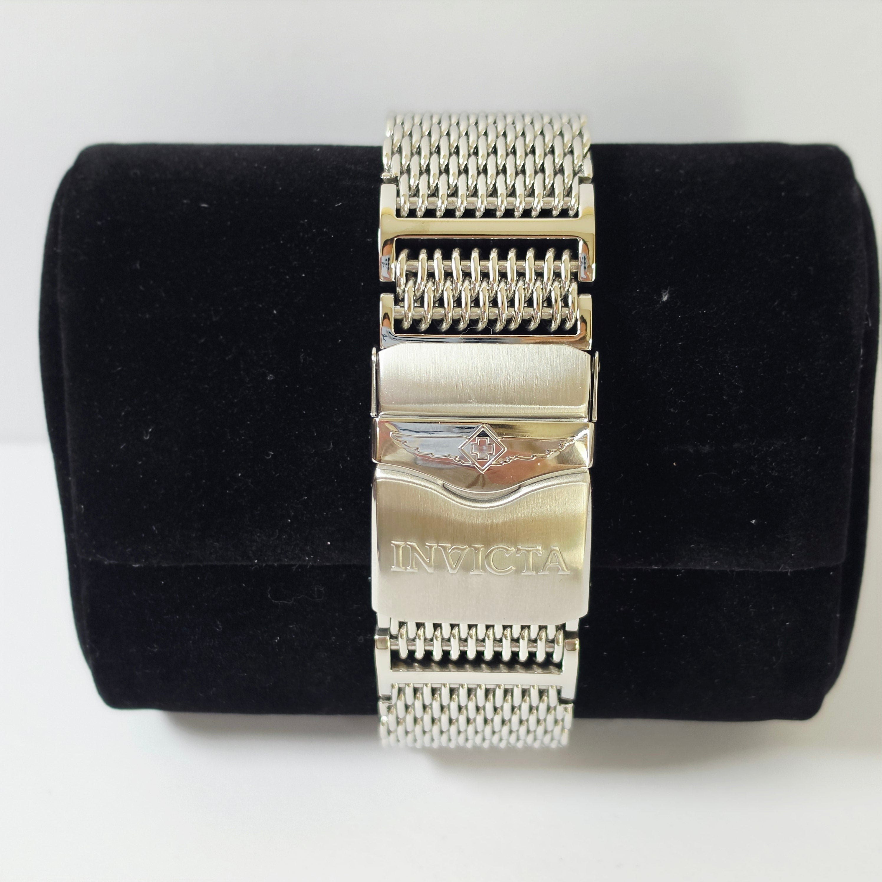 A silver stainless steel mesh watch band with a brushed metal clasp engraved with the brand name 'INVICTA', displayed on a black velvet cylindrical stand against a white background.