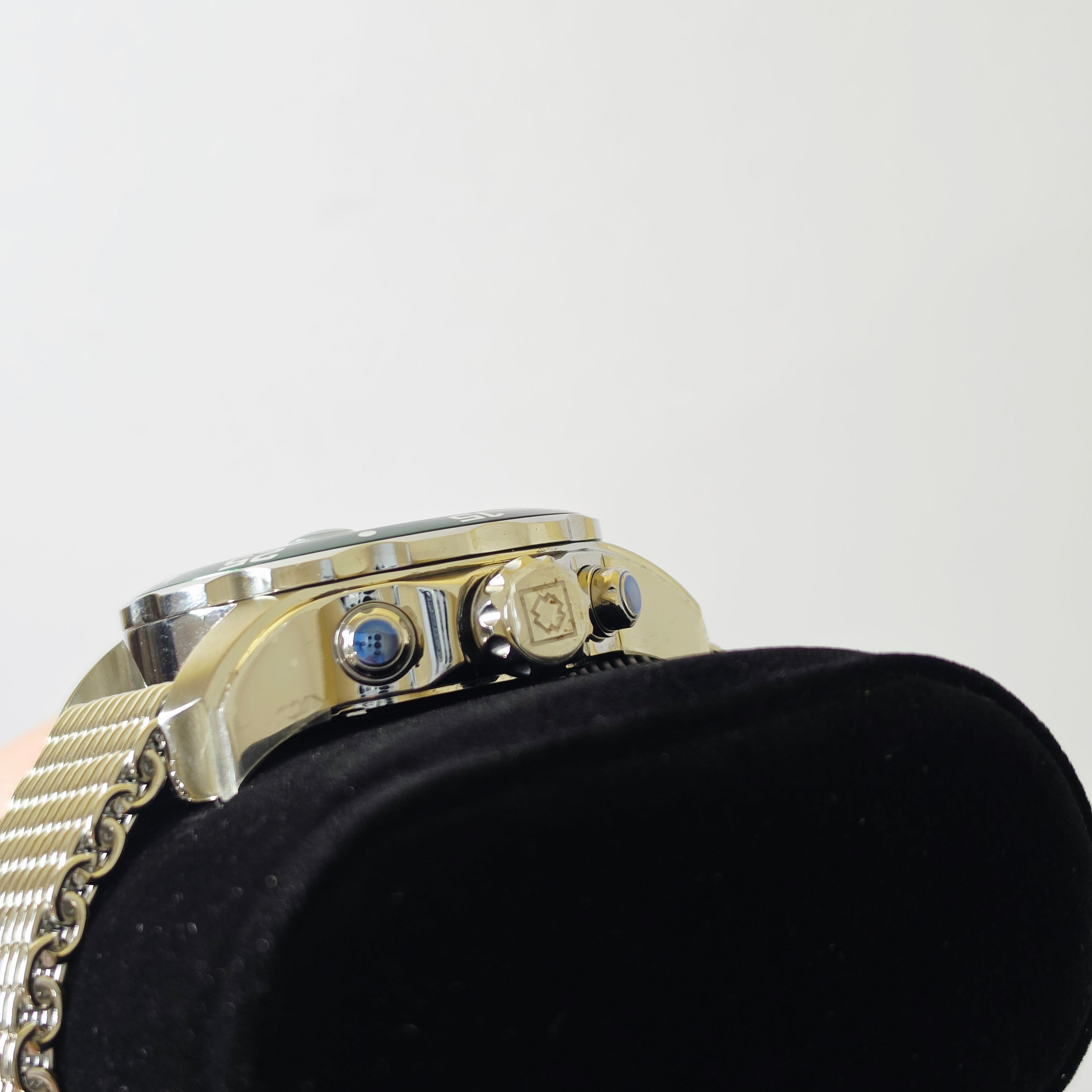 Close-up of a gold-tone watch with a mesh metal band, resting on a black display cushion against a plain light background.