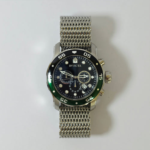 An Invicta wristwatch with a silver mesh metal bracelet, a black dial, and a black bezel with a green accent, photographed against a light gray background.