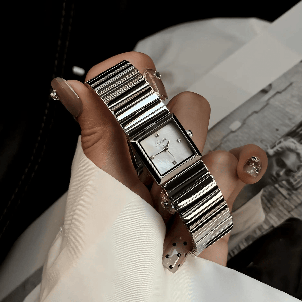 Square two-tone bracelet watch with crystal crown accent, close-up in hand