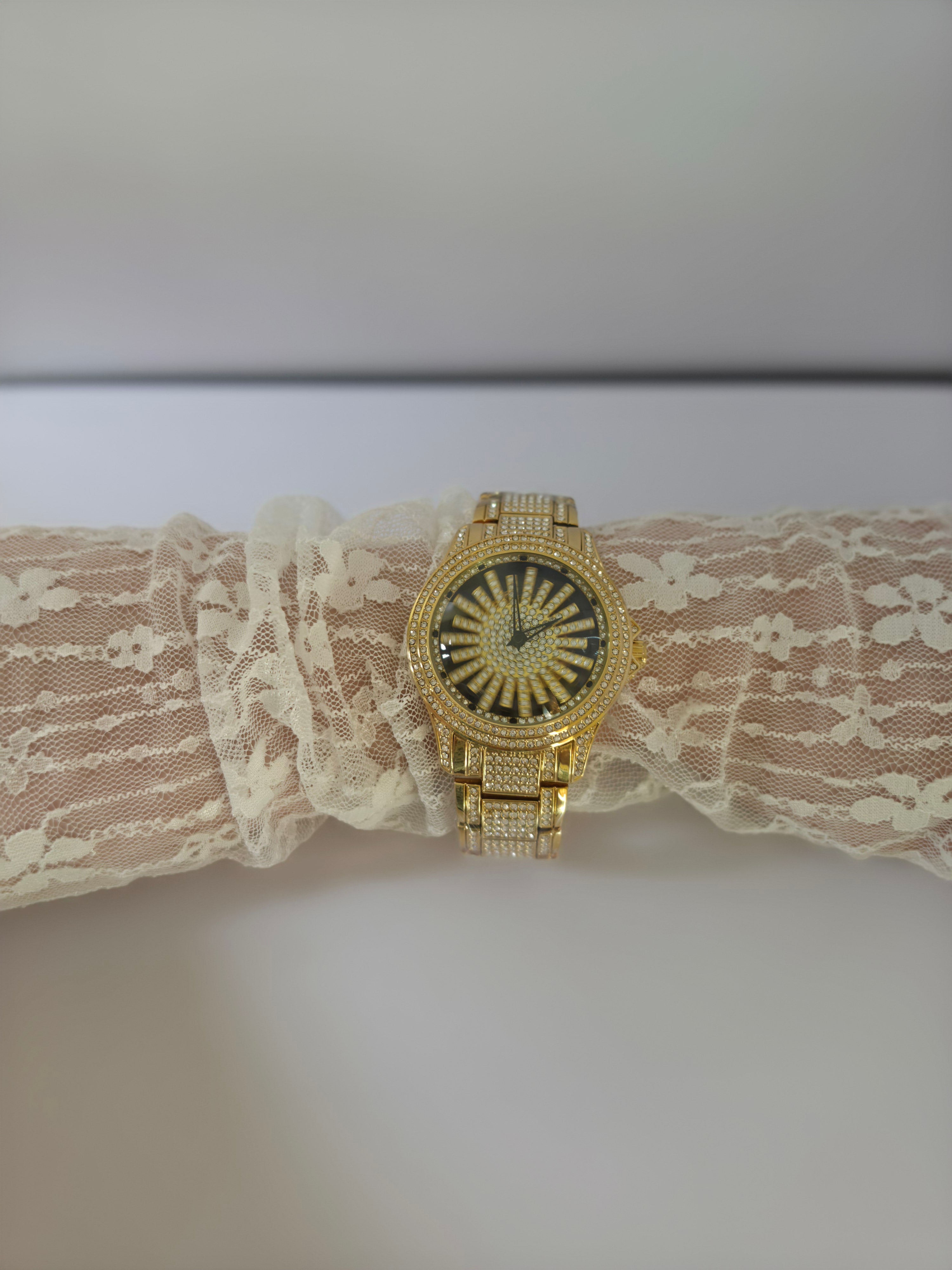 Gold-tone crystal pavé watch draped on lace, dial facing camera