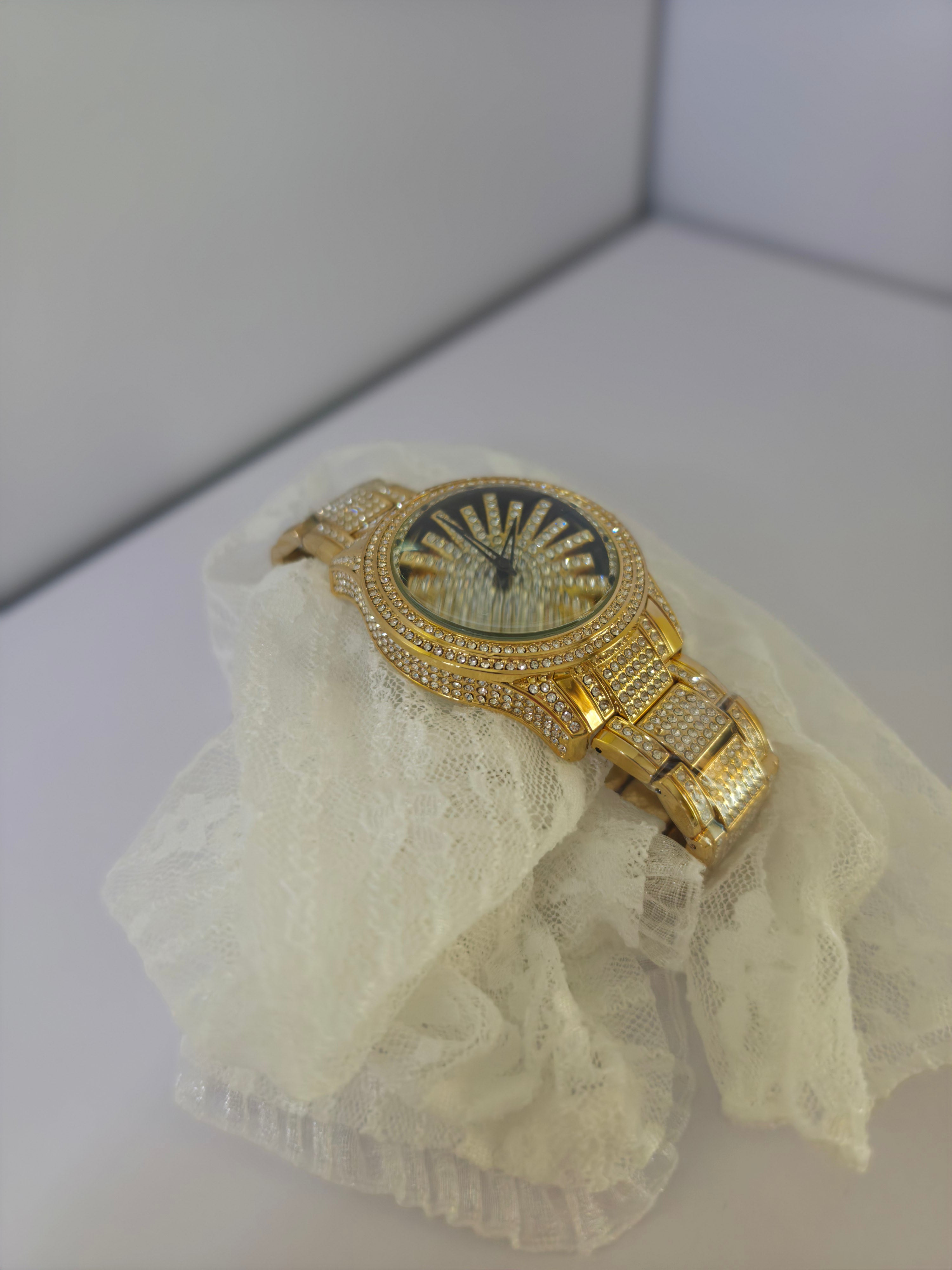 	Gold-tone crystal pavé watch draped over lace fabric, angled view