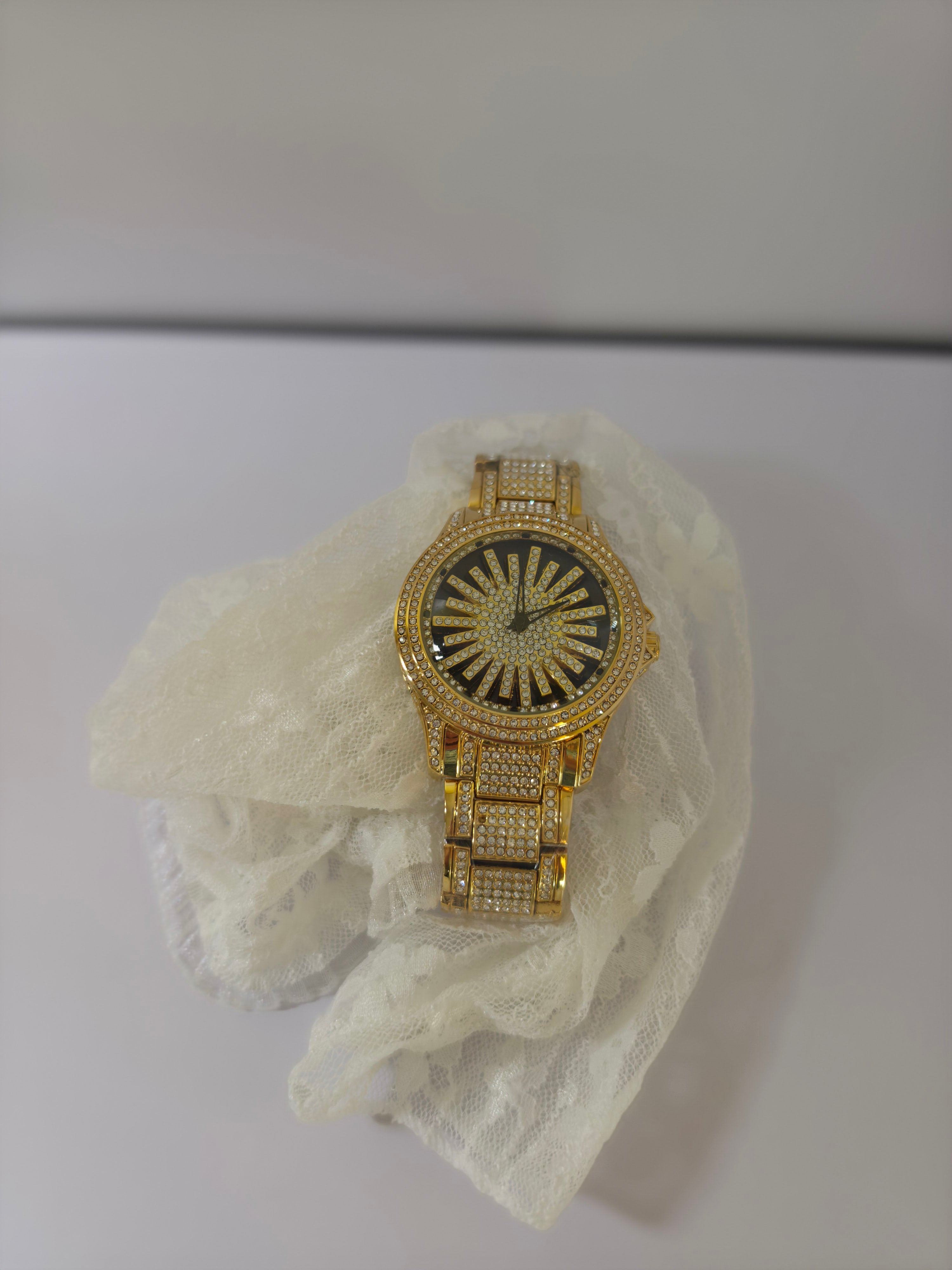 	Gold-tone crystal pavé watch resting on white lace, front angle