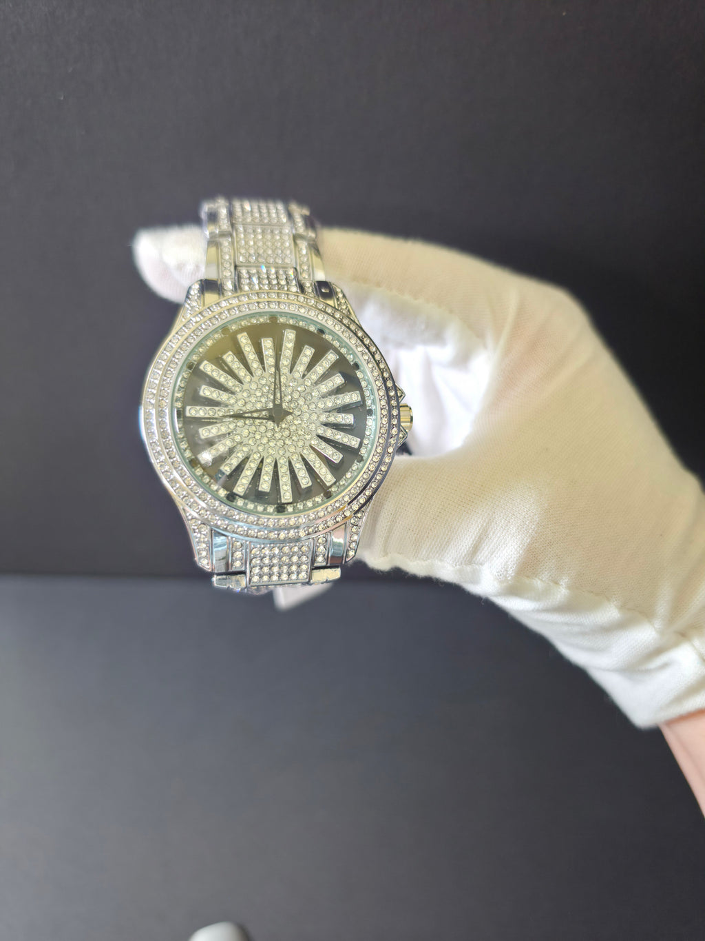 	Close-up of white-gloved hand holding silver-tone crystal pavé watch