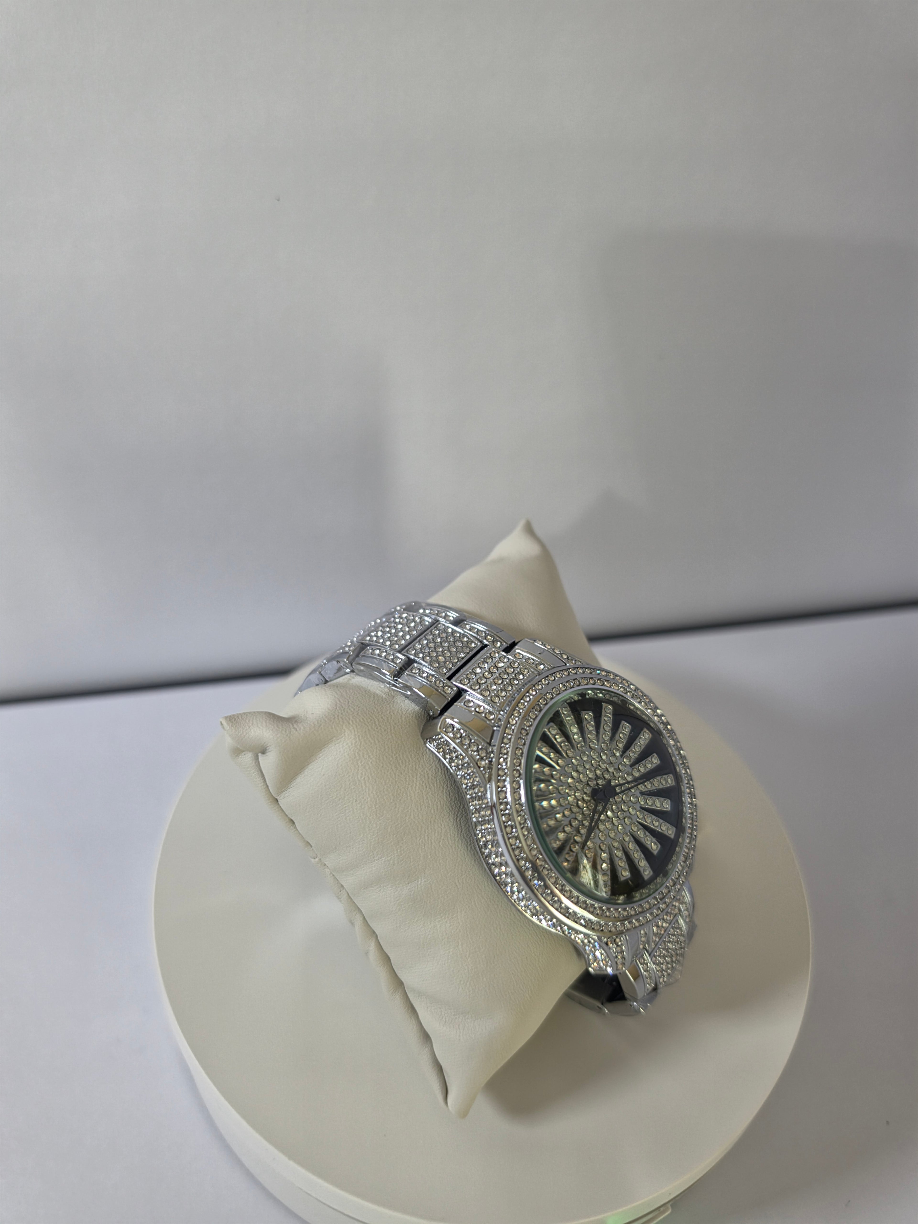 	Silver-tone crystal pavé watch resting on cream pillow, angled view