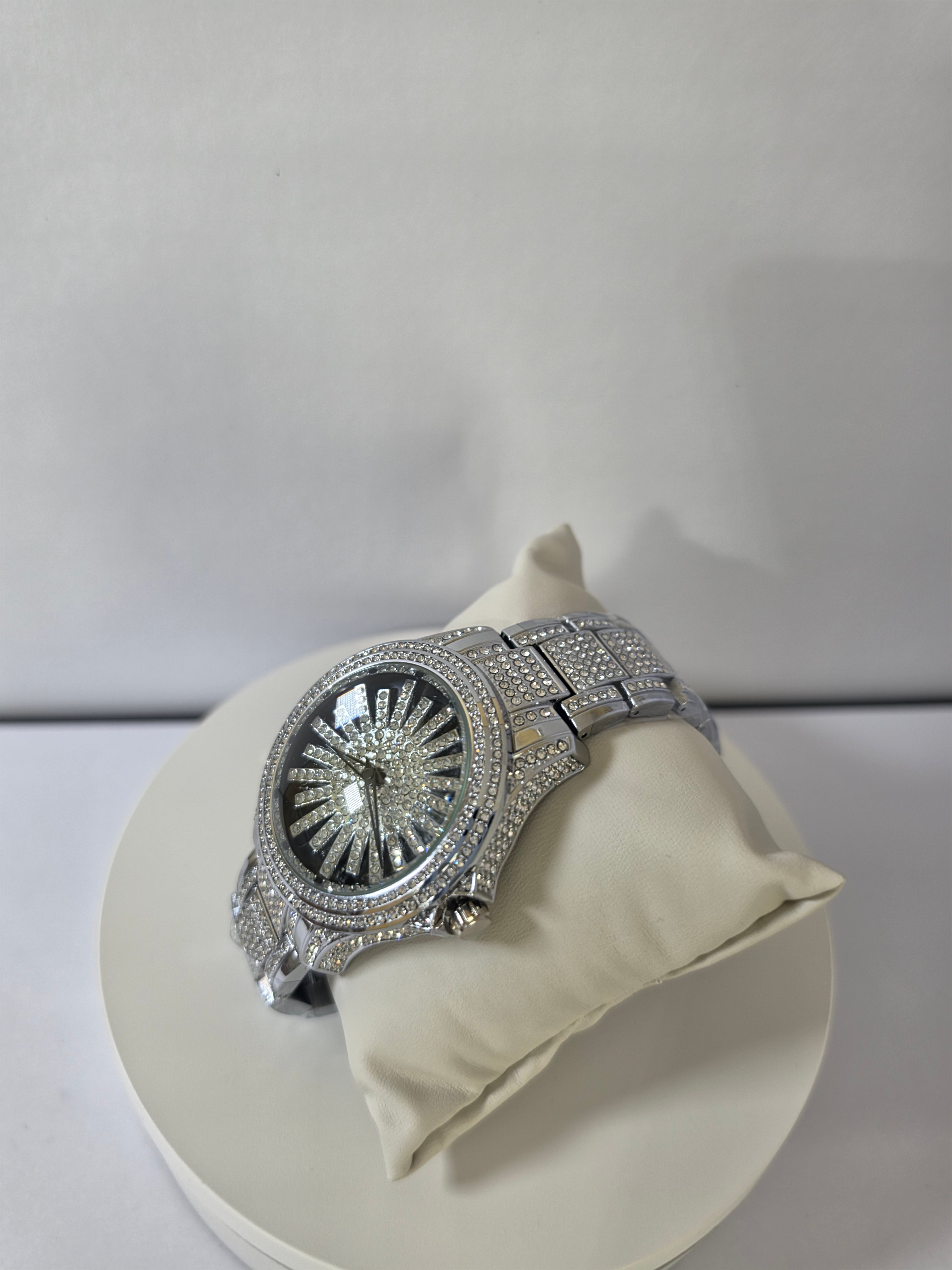 	Silver-tone crystal pavé watch resting on cream pillow, angled view