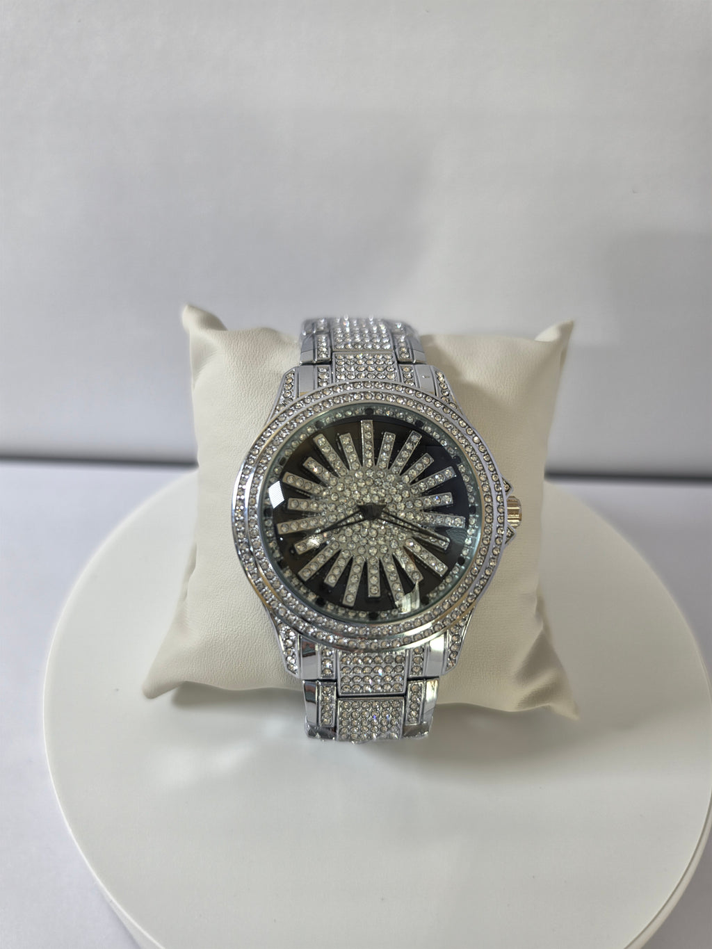 Silver-tone iced-out watch with crystal pavé dial on cream display pillow, top view