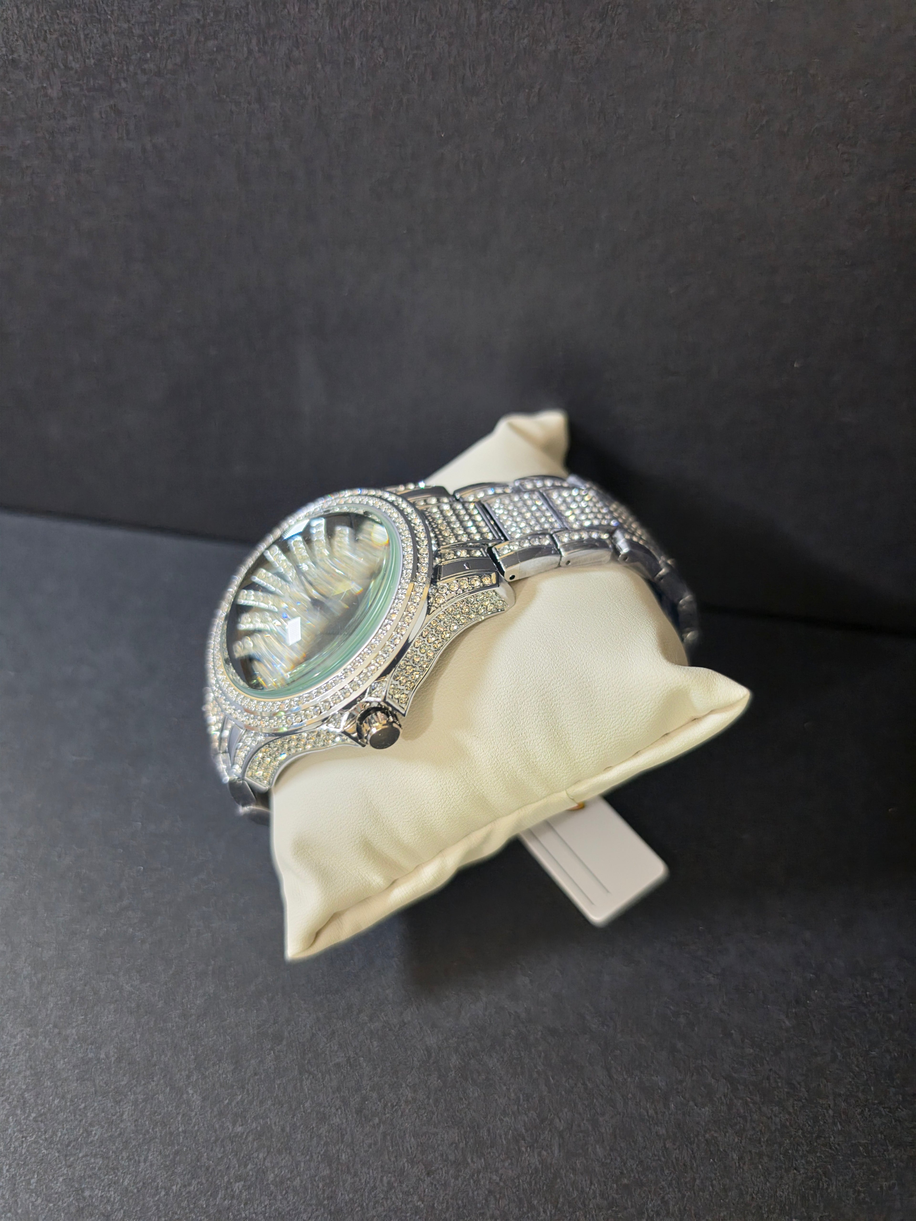 	Silver-tone crystal pavé watch resting on cream pillow, angled view